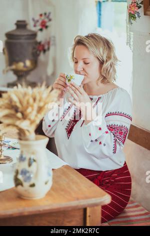 Une belle paysanne ukrainienne boit du thé dans une ancienne hutte ukrainienne Banque D'Images