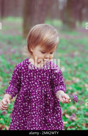 bébé blond dans une robe colorée tenant la fleur dans une verrière de forêt Banque D'Images