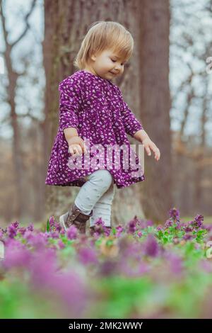 bébé blond dans une robe colorée courant dans une forêt avec des fleurs Banque D'Images
