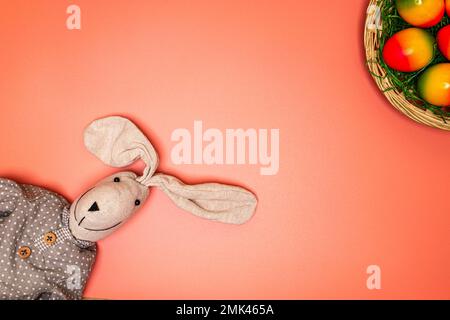 joli lapin de pâques en tissu sur fond orange avec panier de pâques et plusieurs œufs de pâques colorés Banque D'Images