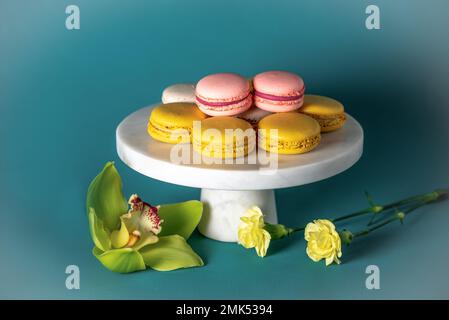 Des gâteaux de macaron français sur un gâteau blanc marbel se dressent sur fond bleu. Blanc jaune, macarons roses.Orchid et sauge. Banque D'Images