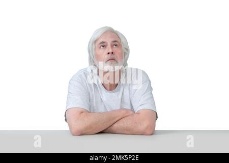 Plan horizontal d'un homme âgé assis à une table en regardant vers le ciel . Isolé sur blanc. Beaucoup d'espace de copie. Banque D'Images