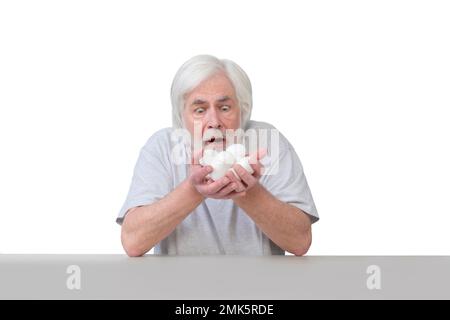 Plan horizontal d'un vieil homme aux cheveux blancs assis à une table étonne de ses mains pleines d'œufs. Isolé sur blanc. Beaucoup d'espace de copie. Banque D'Images