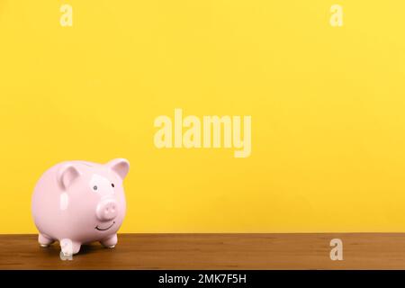 Banc de porc rose sur une table en bois sur fond jaune. Espace pour le texte Banque D'Images