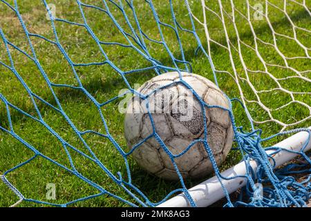 vieux ballon de football dans le filet sur le fond du terrain de football de l'herbe. Jour ensoleillé d'été. Banque D'Images