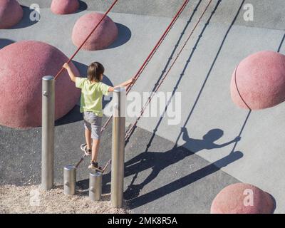 Garçon monte sur une pente de béton de sports et de terrain de jeu modernes pour enfants. Kid surmonte la peur et apprend de nouvelles choses. Activités de loisirs en plein air. Banque D'Images