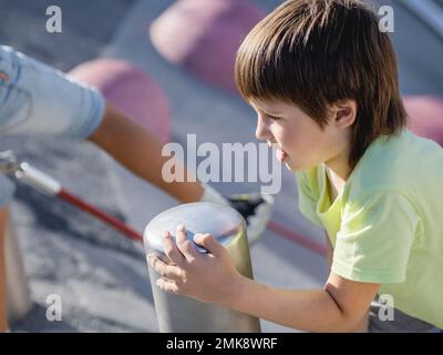 Garçon monte sur une pente de béton de sports et de terrain de jeu modernes pour enfants. Kid surmonte la peur et apprend de nouvelles choses. Activités de loisirs en plein air. Banque D'Images