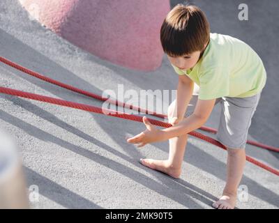 Garçon monte sur une pente de béton de sports et de terrain de jeu modernes pour enfants. Kid surmonte la peur et apprend de nouvelles choses. Activités de loisirs en plein air. Sport l Banque D'Images