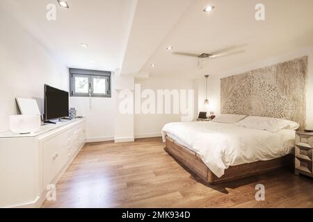 Chambre avec lit double avec couette blanche, parquet en bois sombre, tête de lit en bois de mandala, grand buffet blanc laqué en bois et petite connexion wi Banque D'Images