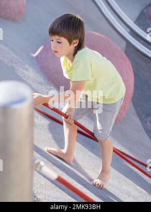 Garçon monte sur une pente de béton de sports et de terrain de jeu modernes pour enfants. Kid surmonte la peur et apprend de nouvelles choses. Activités de loisirs en plein air. Sport l Banque D'Images