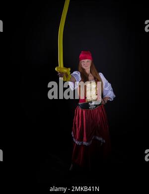 femme aux cheveux longs vêtue comme un pirate dans un costume rouge et avec un ballon jaune en forme d'épée dans sa main photographie d'événements de partie Banque D'Images