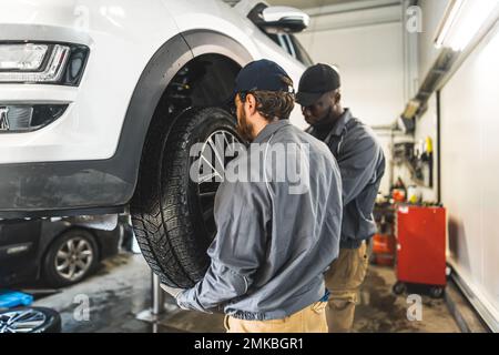 Mécaniciens de voitures remplaçant les roues d'une automobile soulevée dans un poste de réparation. Photo de haute qualité Banque D'Images