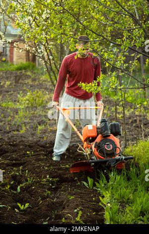 Un fermier travaille dans le champ, labourant la terre avec une charrue sur la ferme. Un charpiller sur une promenade derrière un cultivateur à moteur. Saison de labour. Culte organique Banque D'Images