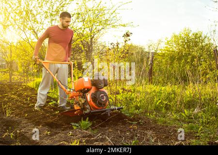 Un fermier travaille dans le champ, labourant la terre avec une charrue sur la ferme. Un charpiller sur une promenade derrière un cultivateur à moteur. Saison de labour. Culte organique Banque D'Images