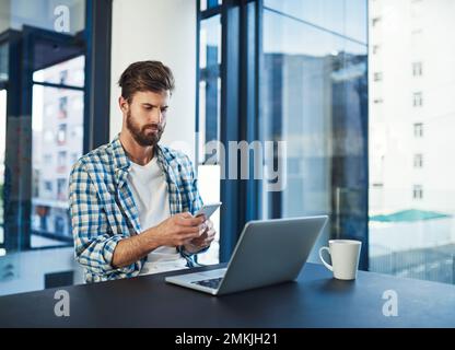 Rester à jour avec son programme. un jeune designer utilisant un téléphone portable dans un bureau moderne. Banque D'Images