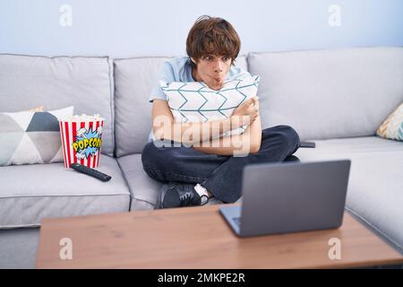 Un jeune homme hispanique regarde un film d'horreur sur l'ordinateur portable, faisant le visage du poisson avec la bouche et les yeux qui s'accroupient, fou et comique. Banque D'Images