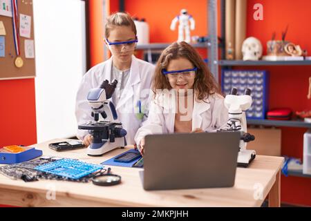Deux enfants élèves utilisant un microscope et un ordinateur portable dans une salle de classe de laboratoire Banque D'Images