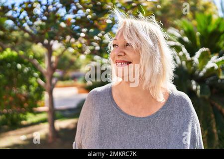 Femme blonde d'âge moyen souriant confiante debout au parc Banque D'Images