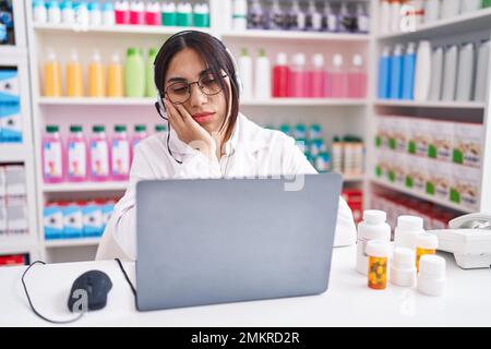 Jeune femme arabe travaillant à la pharmacie en utilisant un ordinateur portable pensant fatigué et ennuyé avec des problèmes de dépression avec les bras croisés. Banque D'Images