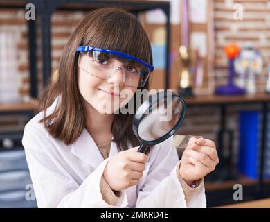 Adorable fille hispanique étudiant regardant l'échantillon en utilisant la loupe dans la salle de classe de laboratoire Banque D'Images