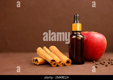 Huile essentielle, cannelle, pomme et poivre sur fond marron. Produit de beauté médical cosmétique en flacon de verre brun avec pipette pour aromatherap Banque D'Images