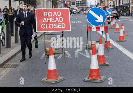 Homme d'affaires se dirige à travers les cônes de trafic lors d'une fermeture de route dans le centre de Londres, Angleterre, Royaume-Uni Banque D'Images