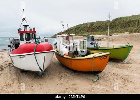 Danemark, Jutland du Nord, Lönstrup : trois bateaux de pêche colorés remorqués sur la plage de sable sous un ciel couvert. Banque D'Images