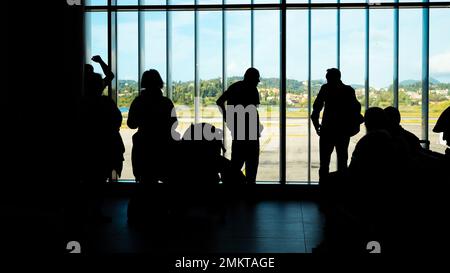 Kerkyra, Grèce - 09 29 2022: Silhouettes de personnes avec des bagages à main et billets d'entrée en attente de départ de leur avion dans le salon de l'aéroport. Banque D'Images