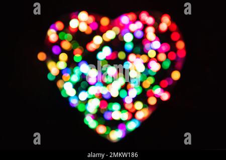 Cercles de lumière multicolores avec effet bokeh en forme de cœur sur fond noir (toile de fond pour le jour de la Saint-Valentin) Banque D'Images