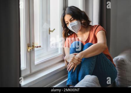 Jeune femme arabe déprimé portant un masque de protection assis près du vent à la maison Banque D'Images