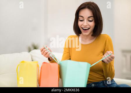 Une jeune femme surjoyée reçoit des achats, l'intérieur de la maison Banque D'Images