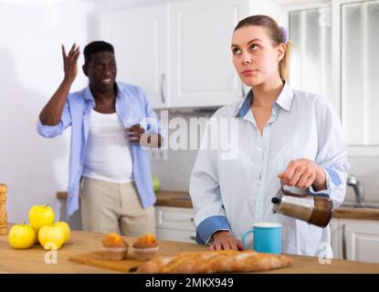 Une jeune femme contrariée verse du café dans une tasse sur fond de mari insatisfait Banque D'Images