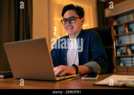 Beau jeune heureux spécialiste INFORMATIQUE travaillant sur l'ordinateur au bureau Banque D'Images