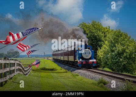 Strasburg, Pennsylvanie. 48 juin 2021 - vue de Thomas le train tirant des voitures de tourisme tout en passant les drapeaux américains sur une clôture le jour du soleil Banque D'Images