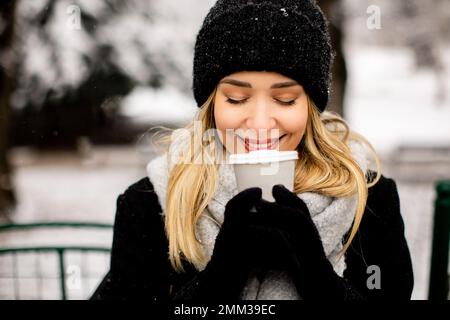 Jolie jeune femme n vêtements chauds appréciant dans la neige avec une tasse à café à emporter Banque D'Images