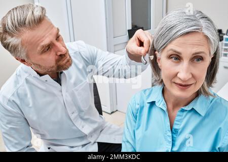 L'audiologiste s'adapte sur l'oreille d'une femme mûre lors de sa visite au centre d'audiologie. Solutions auditives pour adultes Banque D'Images