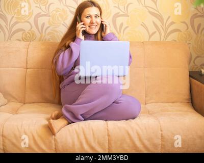 Une fille en costume violet avec un ordinateur portable sur le canapé. La communication dans les médias sociaux Banque D'Images