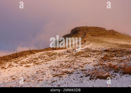 En regardant vers le sommet de la montagne de Pen-y-ghent au lever du soleil, la brume se dissipe et la lumière prend le sommet escarpé d'un Yorkshire Dales Na enneigé Banque D'Images