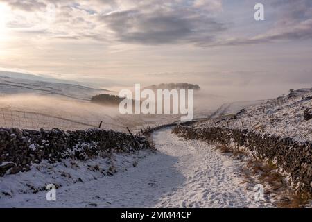 Descente du chemin fortifié vers Horton-in-Ribblesdale depuis la montagne de Pen-y-ghent lors d'une journée d'hiver enneigée avec une légère brume et du soleil dans le Yorkshire Da Banque D'Images