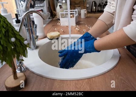 Nettoyage de l'évier dans la cuisine avant les vacances de Noël et du nouvel an. Mains dans des gants et une éponge, détergent, poudre sèche. Décoration festive dans le kitc blanc Banque D'Images