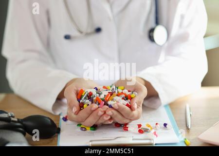 Médecin avec stéthoscope tient un tas de pilules multicolores dans ses mains de près. Banque D'Images