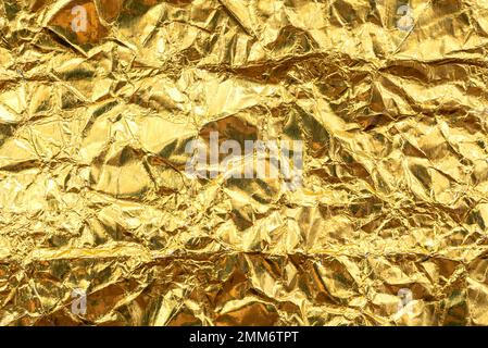Texture luxueuse en papier d'aluminium doré. Feuille jaune émietté avec éraflures et vagues Banque D'Images