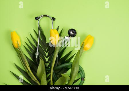 Bouquet de fleurs et stéthoscope sur fond vert, un lieu pour le texte, le joyeux jour des médecins, la semaine des infirmières et d'autres vacances médicales. Banque D'Images