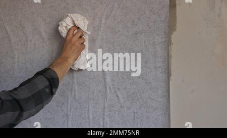 coller le papier peint gris sur le mur et lisser les rides sur la surface avec un tissu en coton blanc, la main d'un homme lisse les bosses Banque D'Images