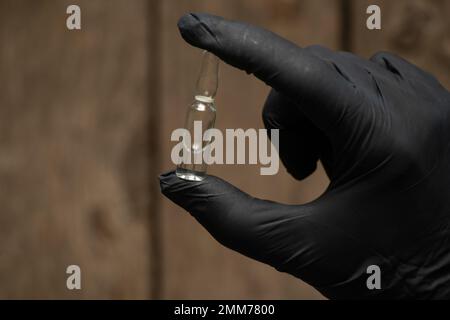 la main dans les gants tient une ampoule avec le médicament Banque D'Images