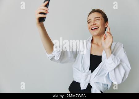 Une jeune fille blogger prend des photos et des pousses. elle-même sur la vidéo sur son téléphone pour le contenu de médias sociaux, blogueur vidéo, se selfie contre un mur blanc avec Banque D'Images