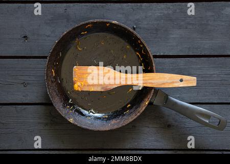 une poêle avec les restes de nourriture et une spatule en bois après la friture est sur la table dans la cuisine, une poêle sale est sur la table Banque D'Images