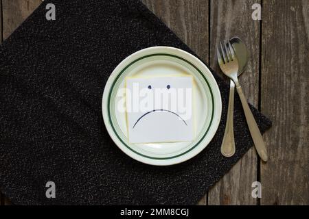 triste udibka dessiné sur un morceau de papier se trouve sur une assiette vide sur la table, tristesse quand il n'y a rien à manger, faim et mauvaise humeur Banque D'Images