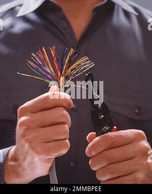 Gros plan des mains du travailleur coupant le fil multirang. Photographie de studio, belle image rétro-éclairée spectaculaire. Banque D'Images