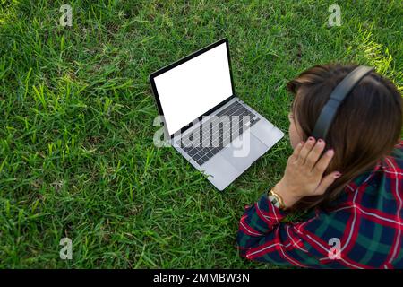 Une fille qui se trouve sur un pré utilise son ordinateur portable et écoute de la musique, écran vierge avec maquette Banque D'Images